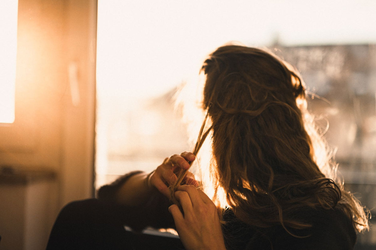 Femme à contre-jour qui passe la main dans ses cheveux emmêlés, à la recherche d'un démêlage plus facile