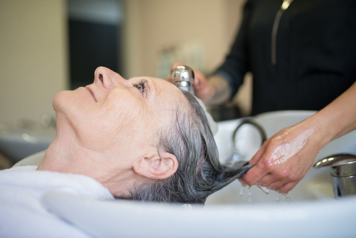 Femme aux cheveux gris savourant un soin capillaire en institut pour raviver l'éclat de sa couleur