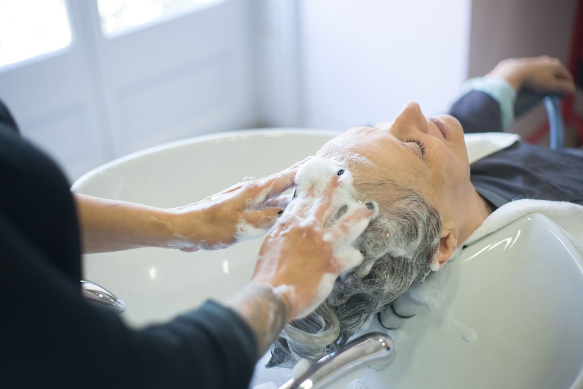 Femme se faisant masser le cuir chevelu lors d'un shampoing en institut