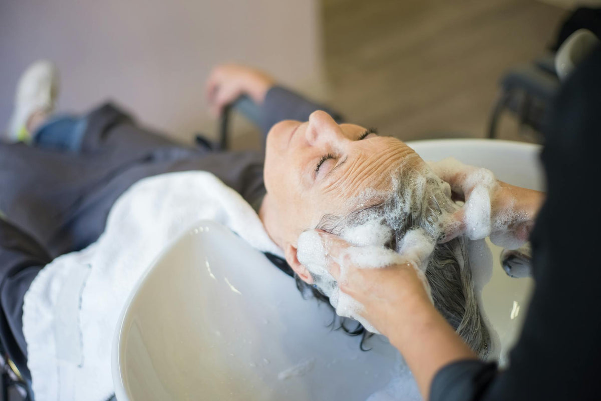 Femme se faisant laver les cheveux en salon, soin capillaire professionnel pour cheveux blonds